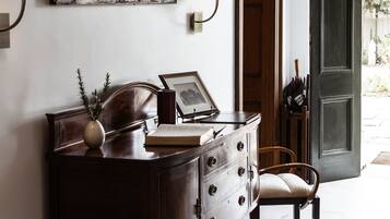 Un bureau en bois avec des tiroirs, un vase et un tableau encadré. Une chaise est placée devant le bureau. Une lampe est fixée au mur, à gauche du bureau.