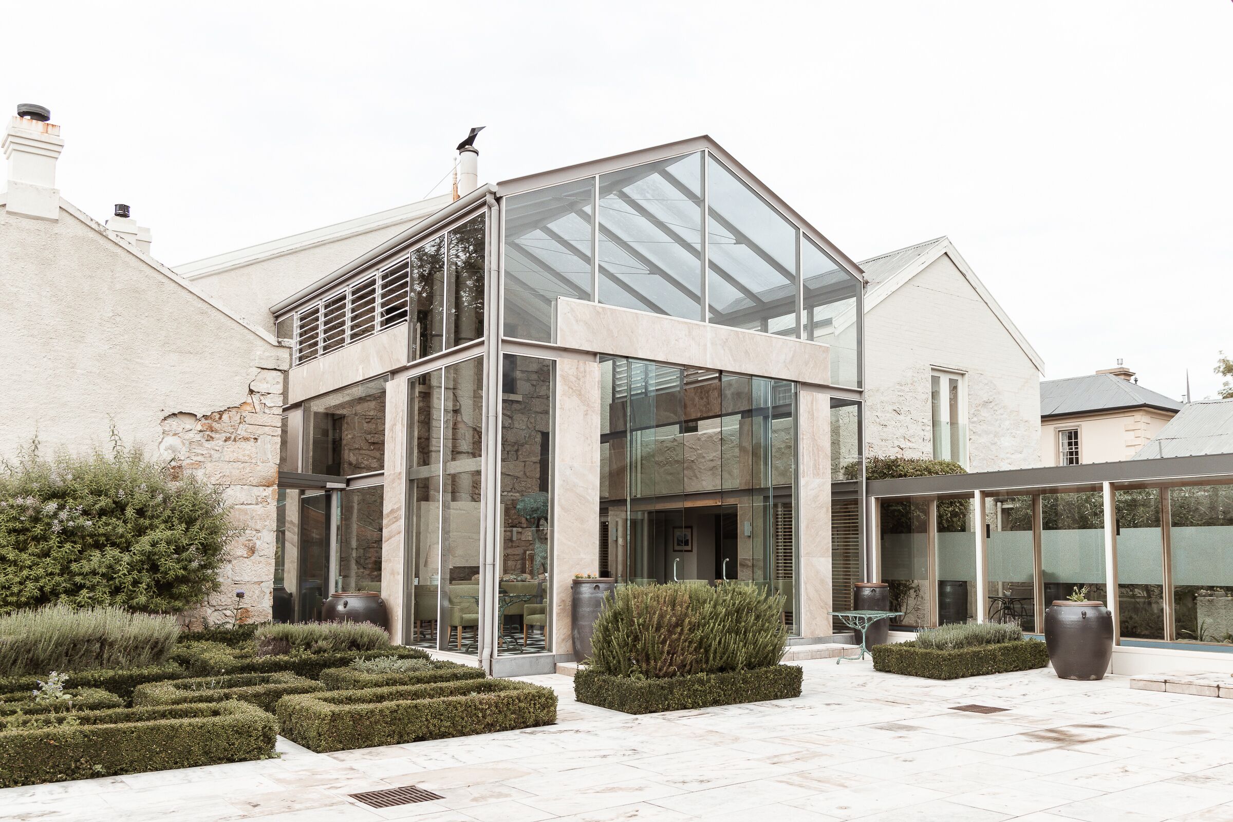 A modern building with large glass windows and a well-maintained garden with hedges and potted plants.