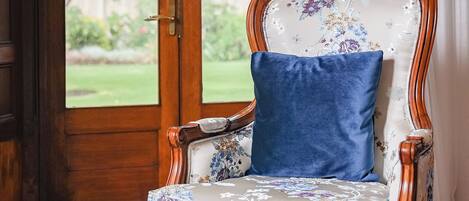 A chair with floral upholstery and a blue cushion, positioned near a window with a view of greenery.