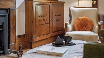 A room with a marble coffee table, a leather armchair with an orange cushion, a wooden cabinet with glass doors, and a floor lamp.