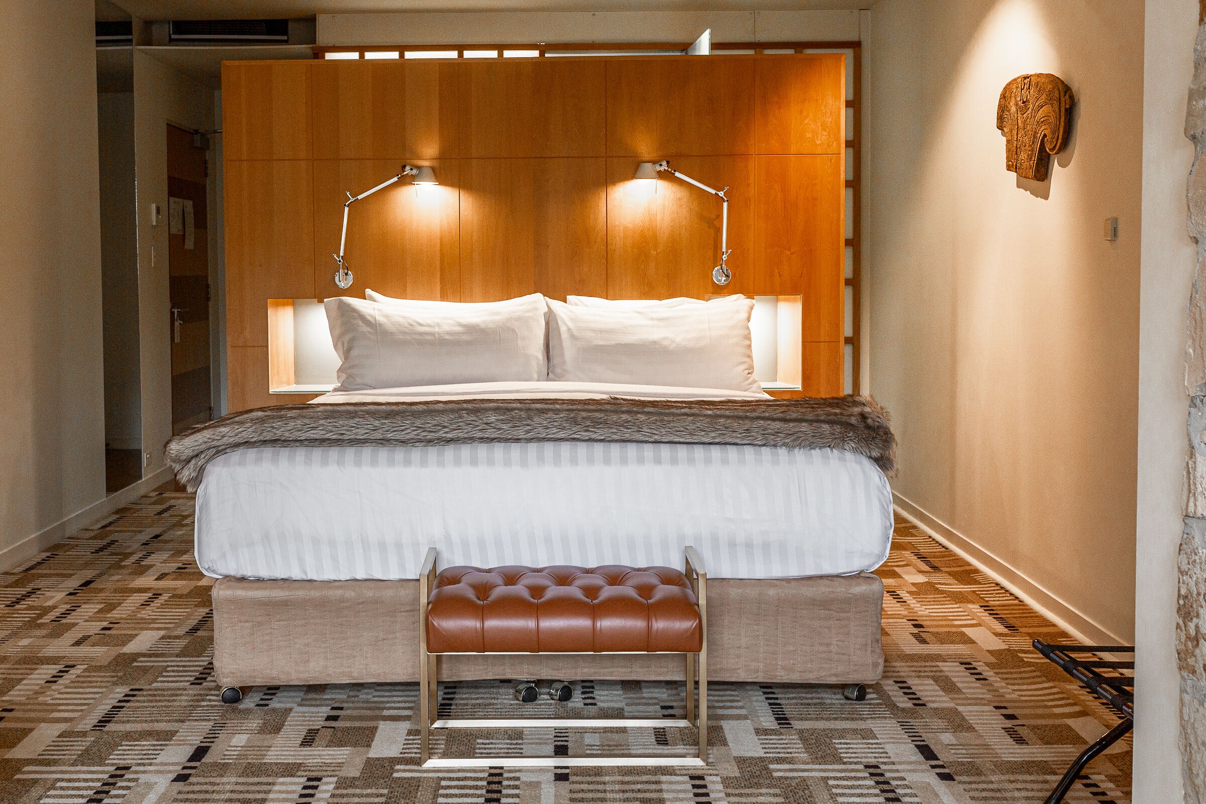 A modern hotel room with a large bed, two bedside lamps, a bench, and a patterned floor.