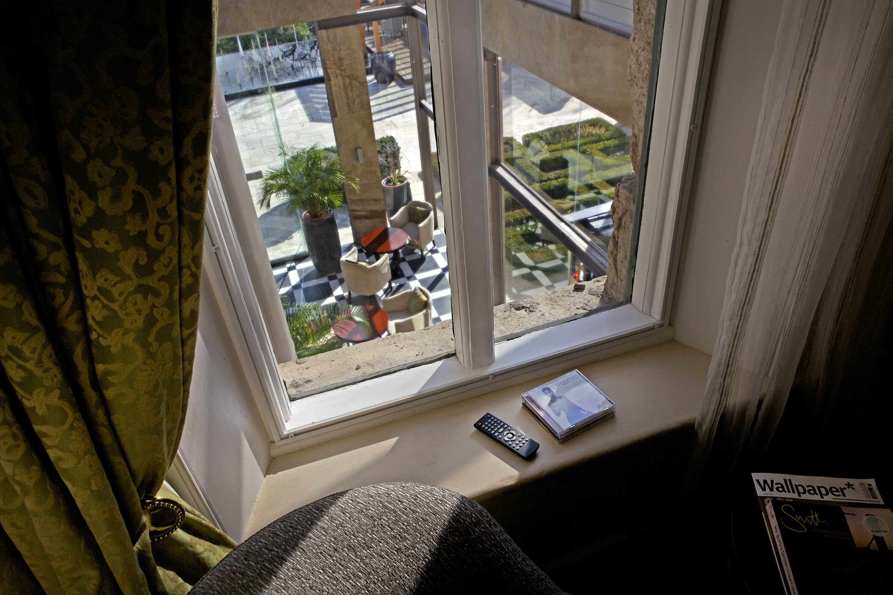 A window with a view of a street, a remote control, and a magazine on the windowsill.
