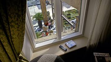A window with a view of a street, a remote control, and a magazine on the windowsill.