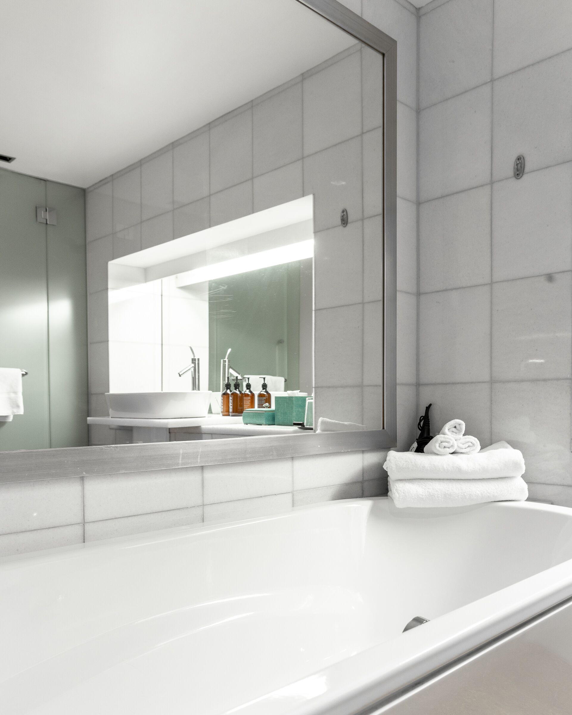 A modern bathroom with a large mirror, a bathtub, and a vanity with toiletries.