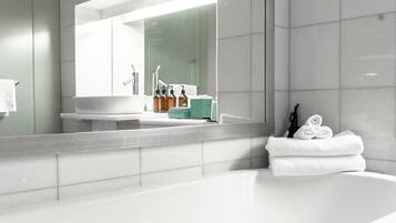 A modern bathroom with a large mirror, a bathtub, and a vanity with toiletries.