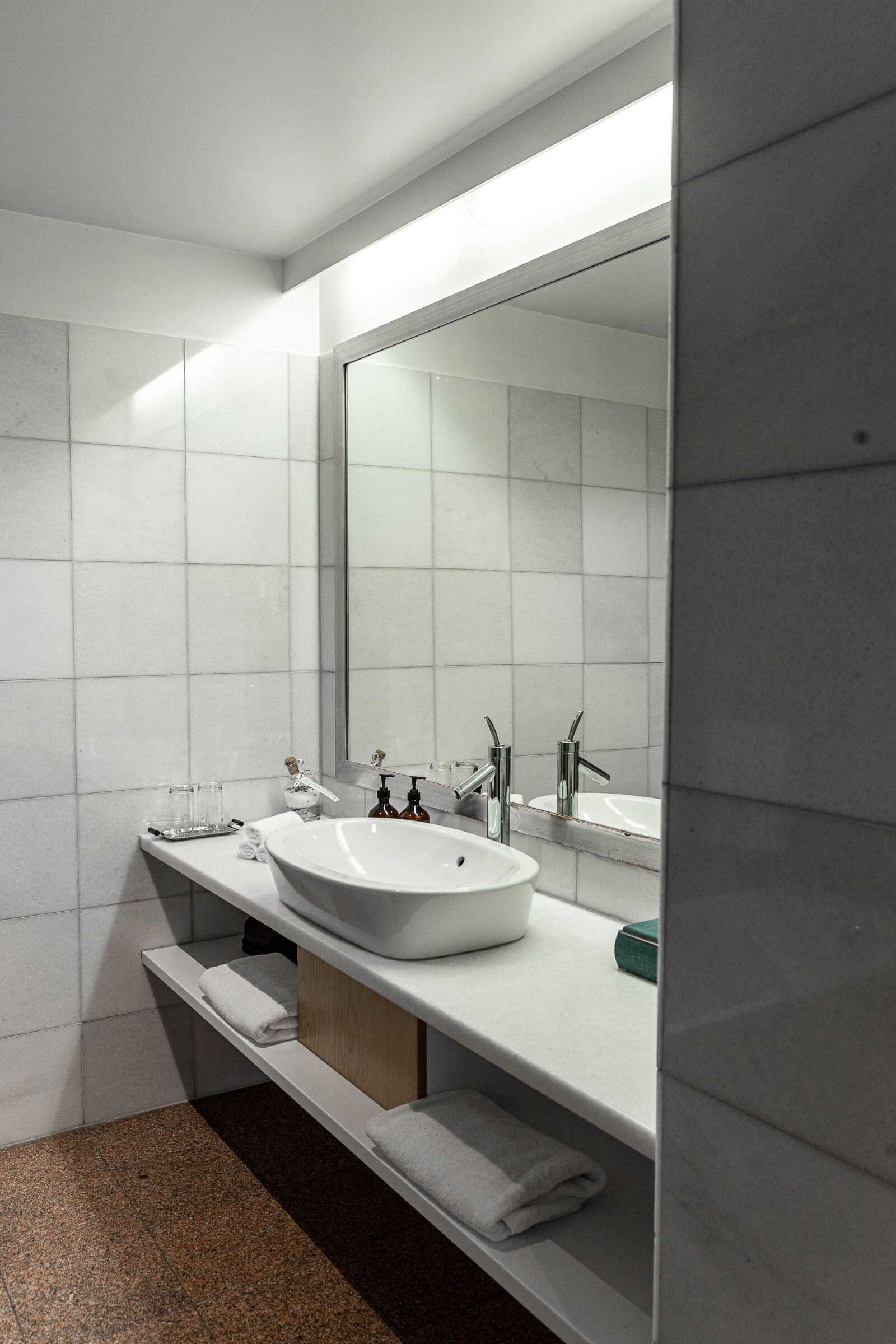 Un baño moderno con un espejo grande, lavamanos blanco y dos grifos.