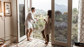 A couple standing by a sliding glass door with a view of a garden and hills. - Islington Hotel (South Hobart)