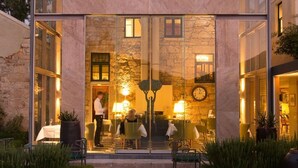 A modern glass conservatory with a stone facade, a dining area with tables and chairs, and a visible clock on the wall. - Islington Hotel (South Hobart)