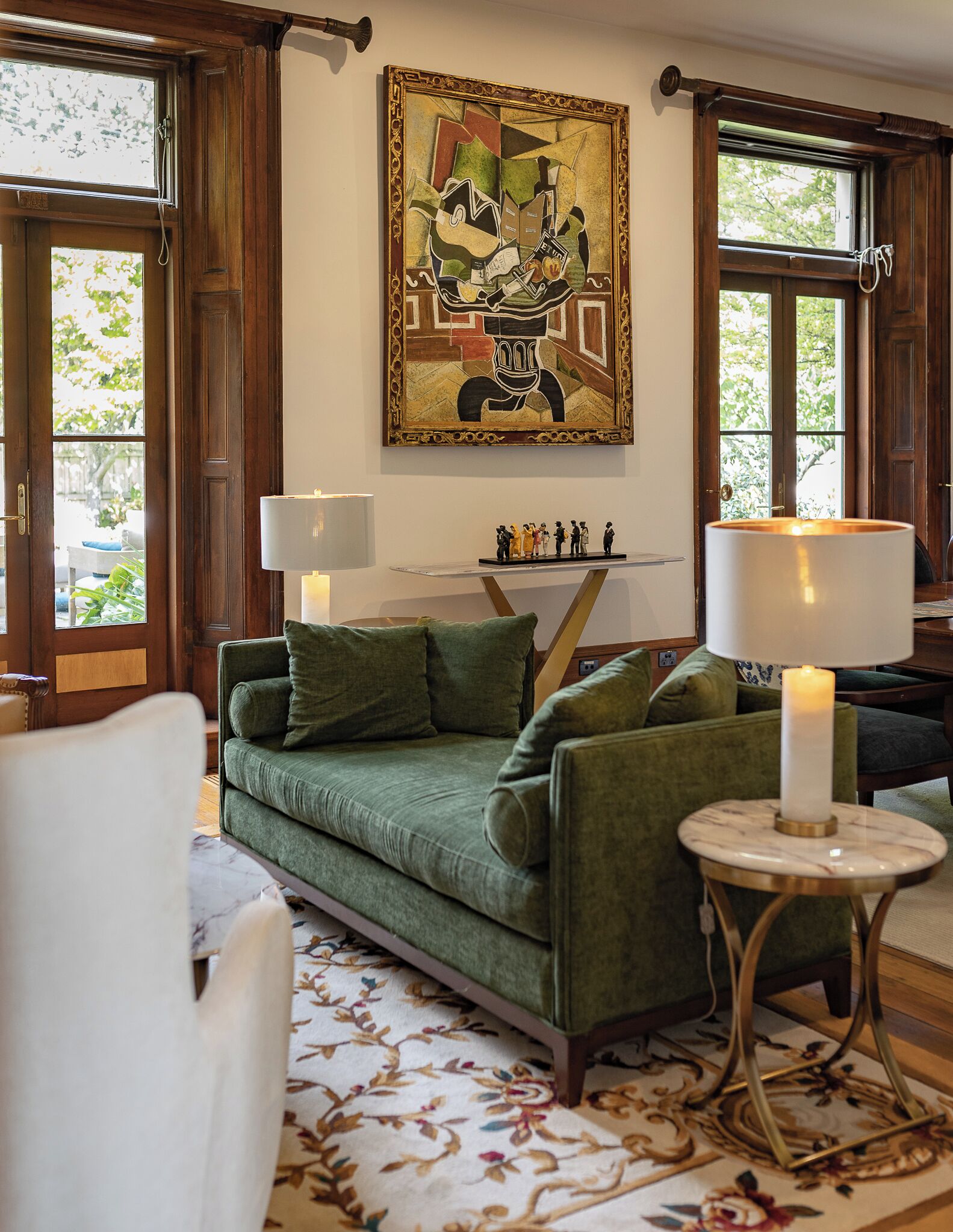 A cozy living room with a green sofa, two lamps, a decorative painting, and a floral rug.