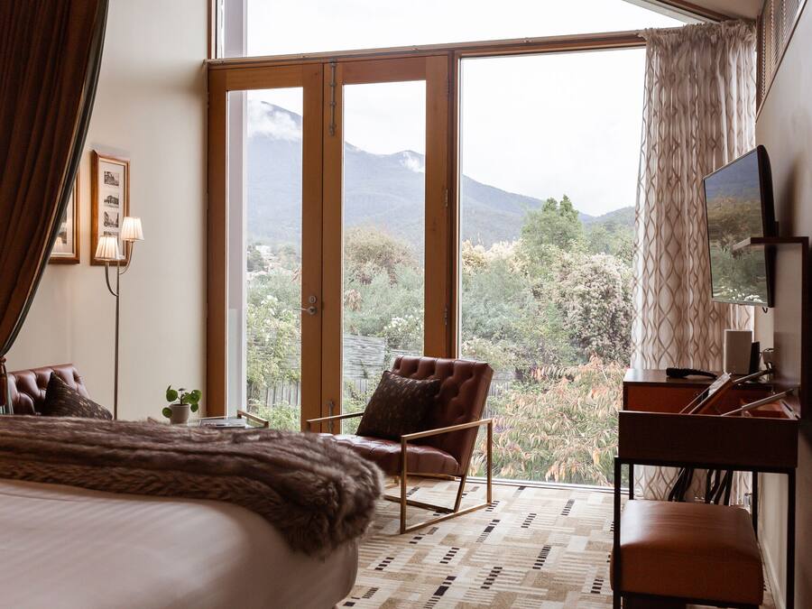 A bedroom with a large bed, a desk, a chair, and a view of mountains through a sliding glass door.
