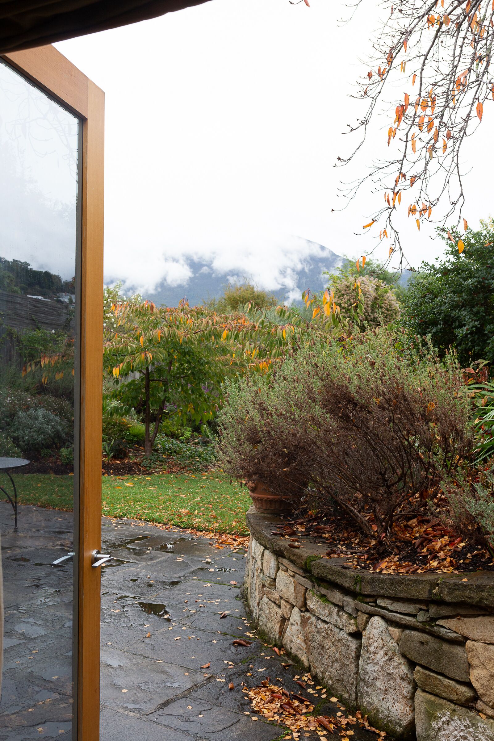 Un chemin de pierre mène à une porte en verre, avec un jardin et une montagne en arrière-plan.