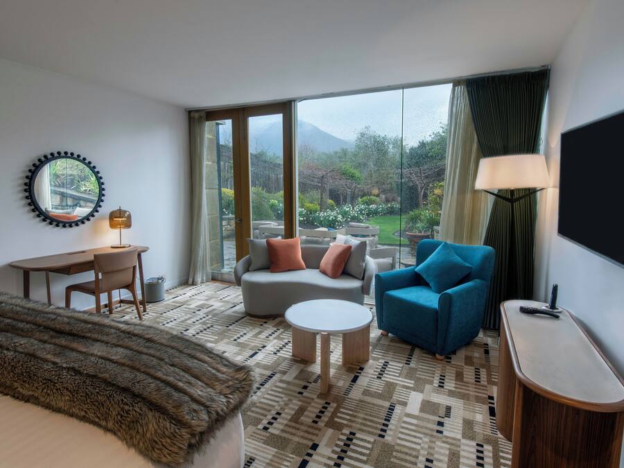 Une chambre d’hôtel comprenant un lit, un bureau, un canapé, un fauteuil bleu, une table basse ronde et un téléviseur.