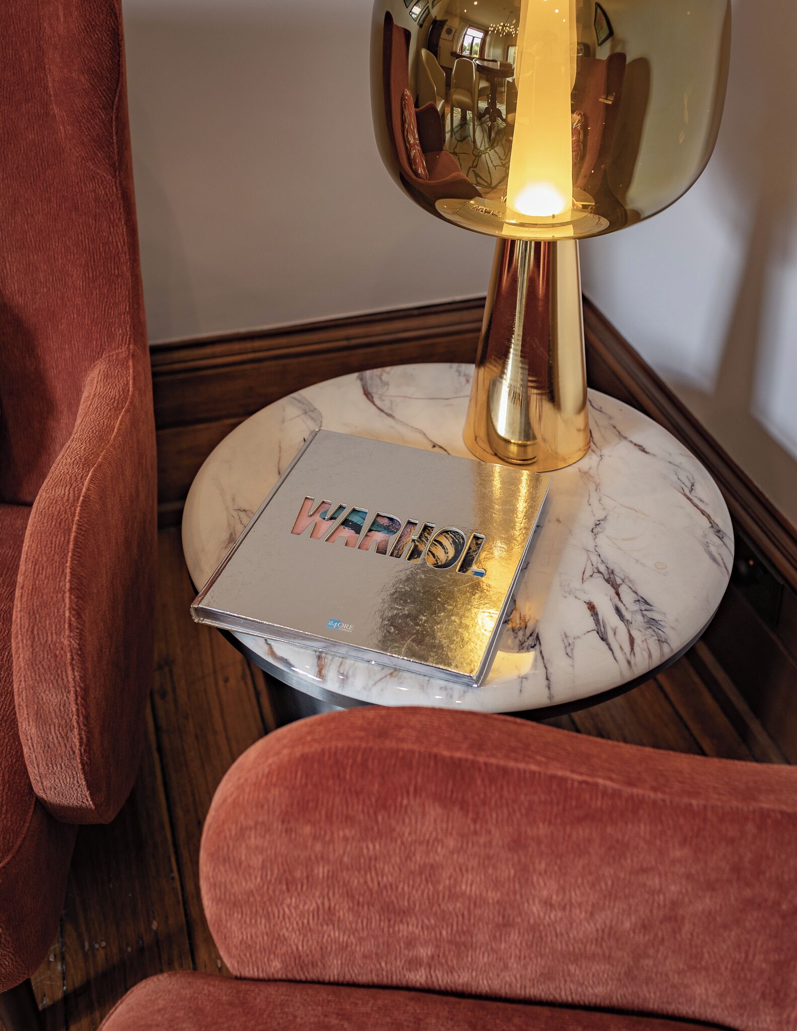 A round marble table with a book titled "WARMING" and a golden lamp.