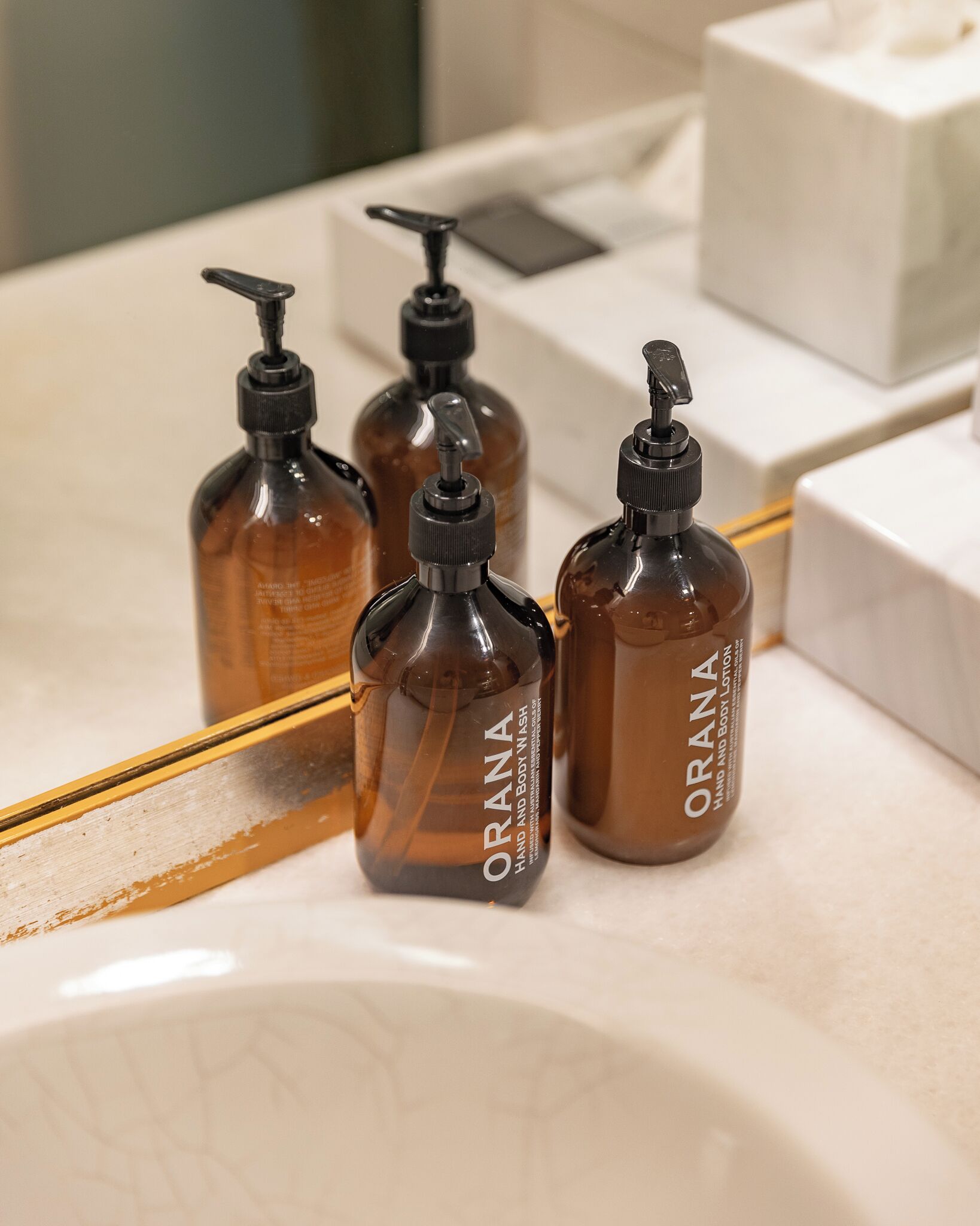 Trois flacons de lotion pour les mains et le corps de la marque ORANA sont posés sur le comptoir d’une salle de bain.