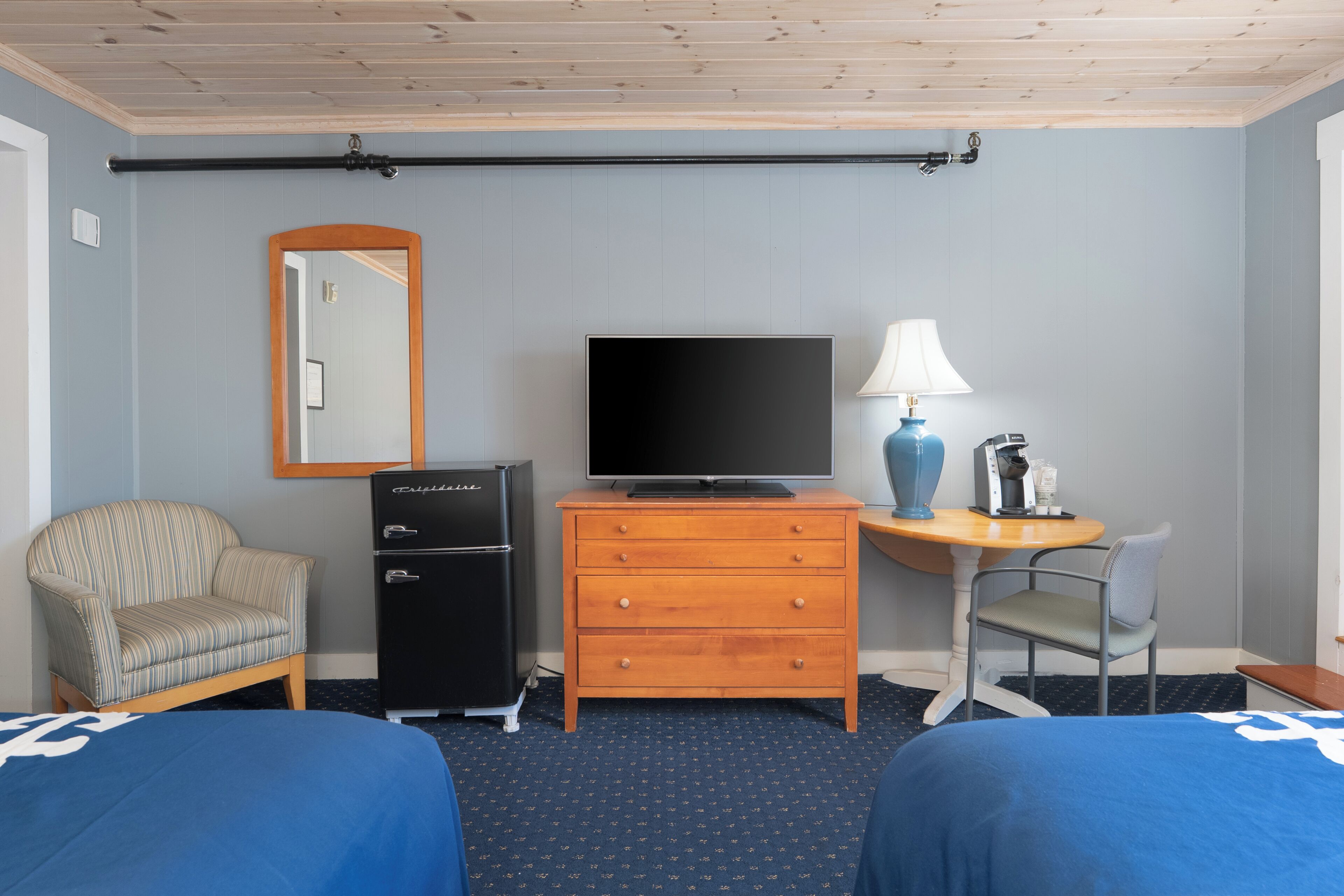 Una habitación de hotel con dos camas, televisión, escritorio con lámpara, una silla y cómoda.