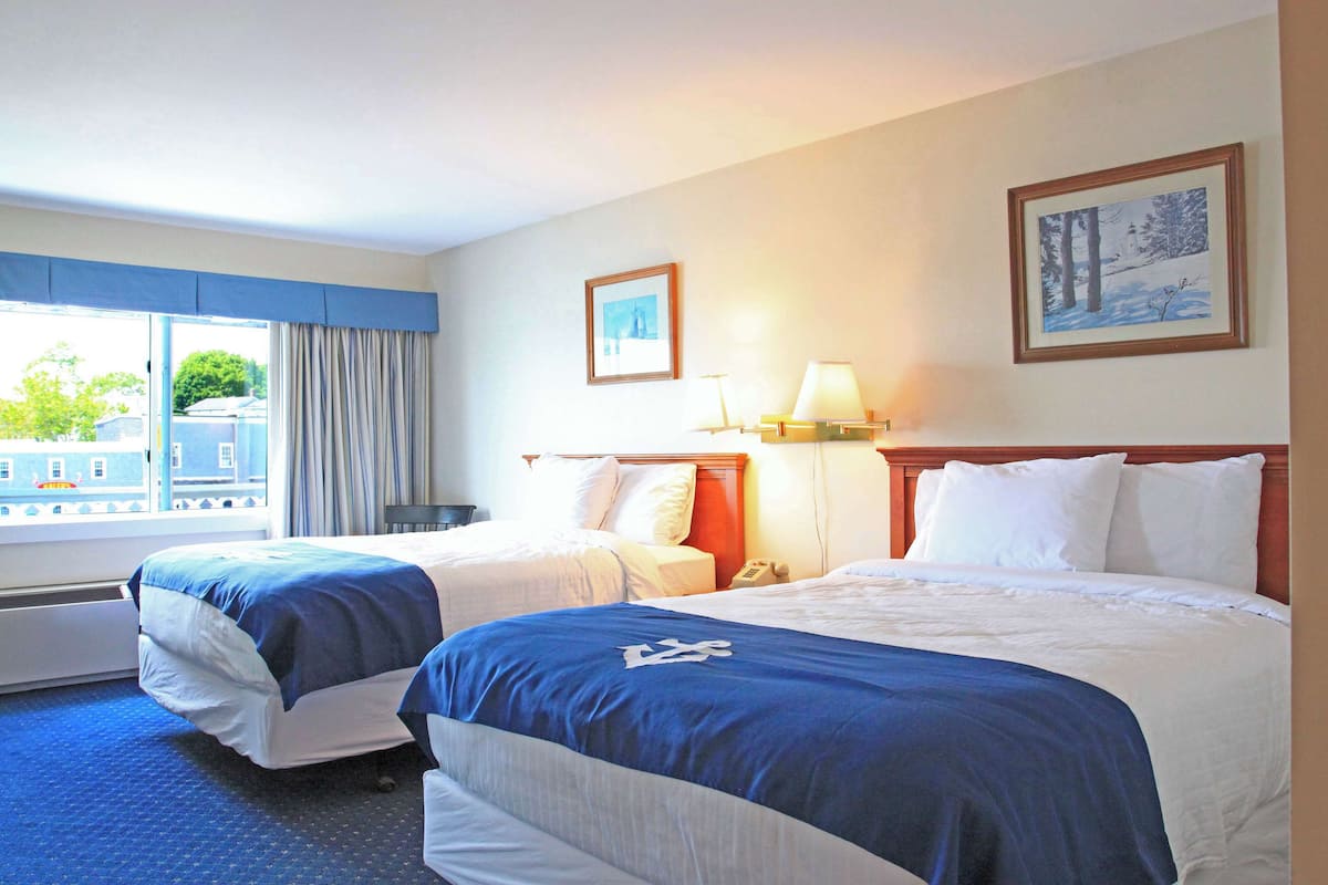 A hotel room with two beds, a window with curtains, a lamp, and two framed pictures on the wall.