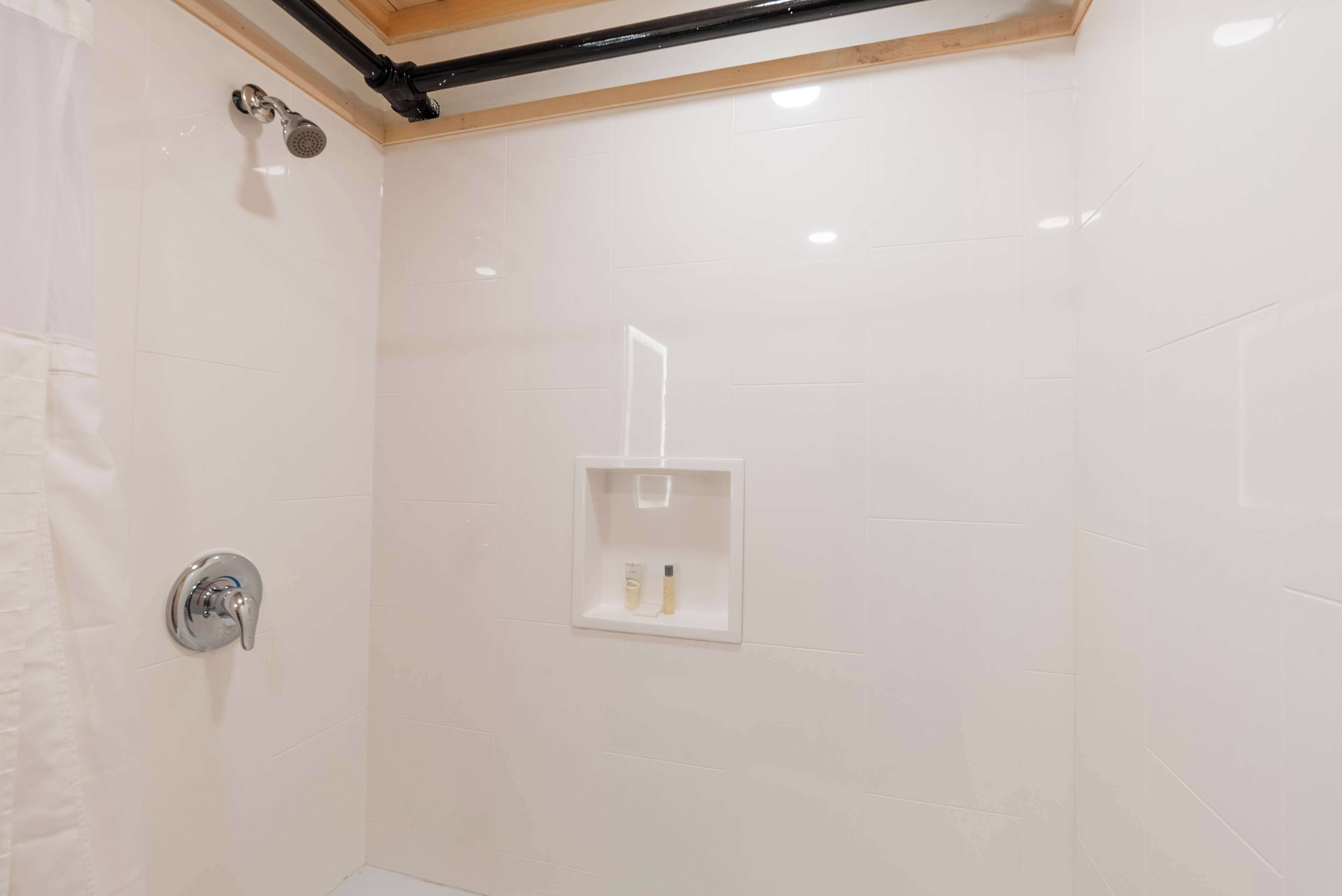 Ein Duschbereich mit Glasabtrennung, einer Duschbrause und einer kleinen Ablage für Toilettenartikel.
