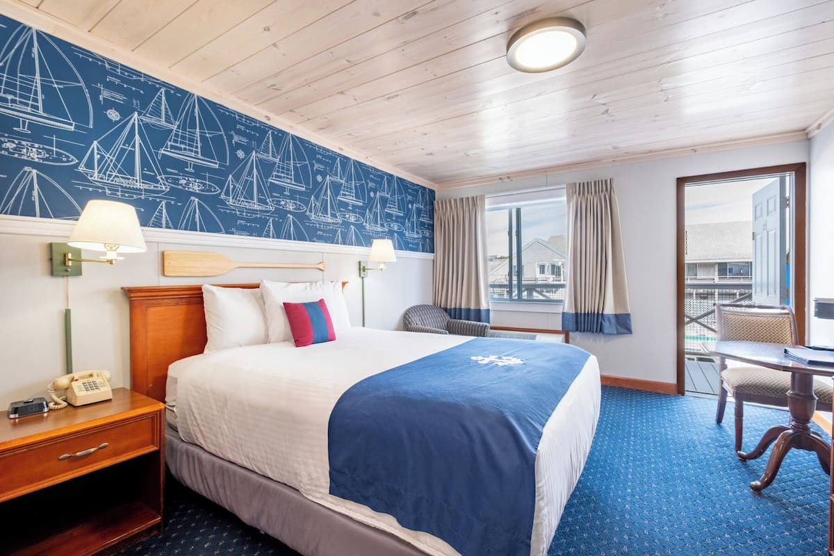 A hotel room with a bed, a desk, a chair, a telephone, a lamp, and a window with curtains.