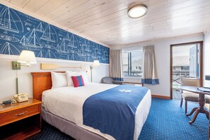 A hotel room with a bed, a desk, a chair, a telephone, a lamp, and a window with curtains. - Fishermans Wharf Inn (Boothbay Harbor)