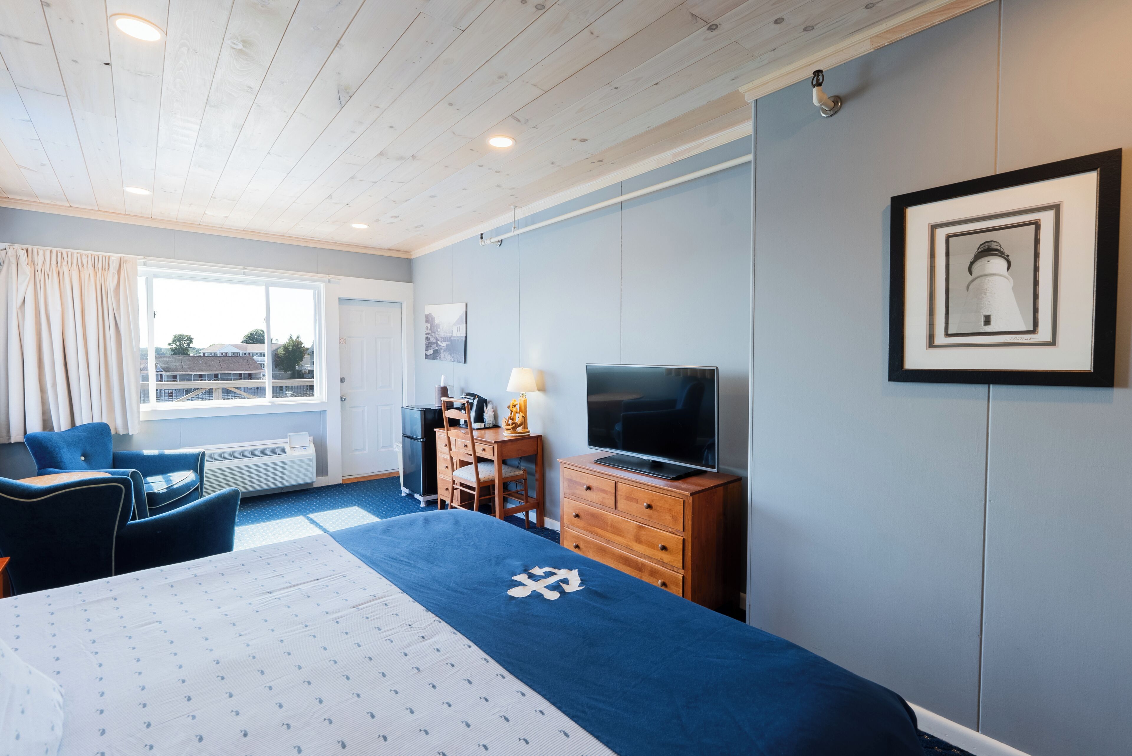 Habitación de hotel con cama, escritorio, silla, cómoda, televisor y un cuadro en la pared.