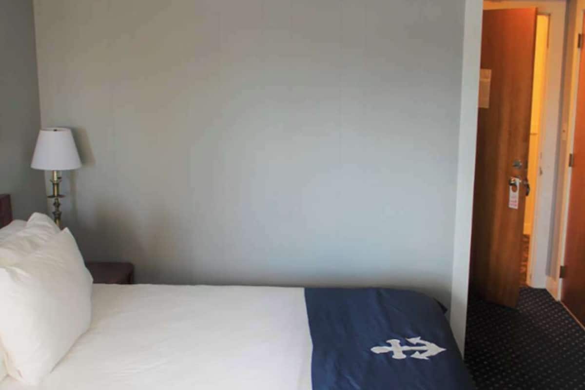 A hotel room with a bed, a nightstand, a lamp, and a door.