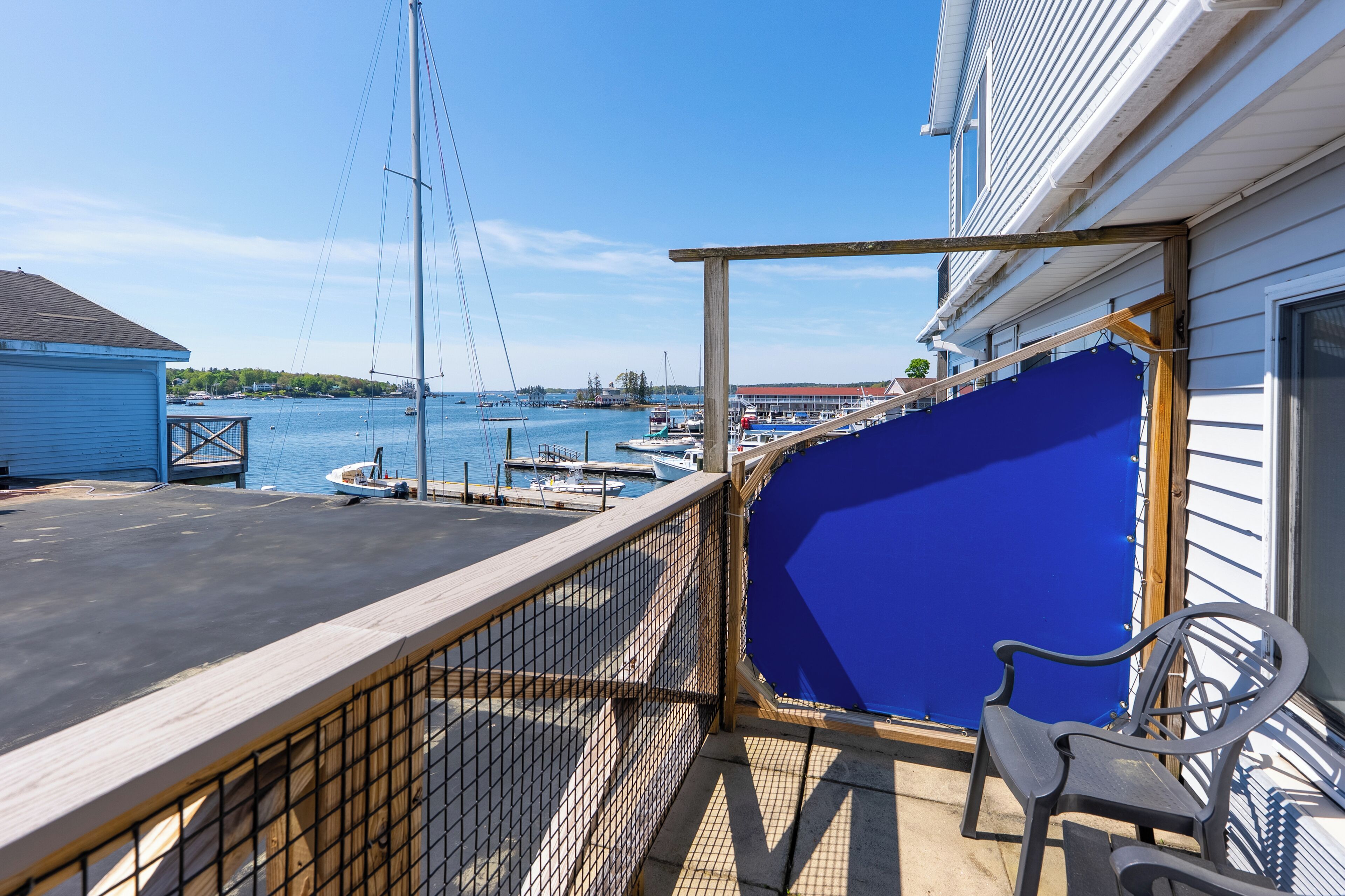 Een balkon met uitzicht op de jachthaven, een stoel en een blauwe zeil afdekking over een deel van de reling.