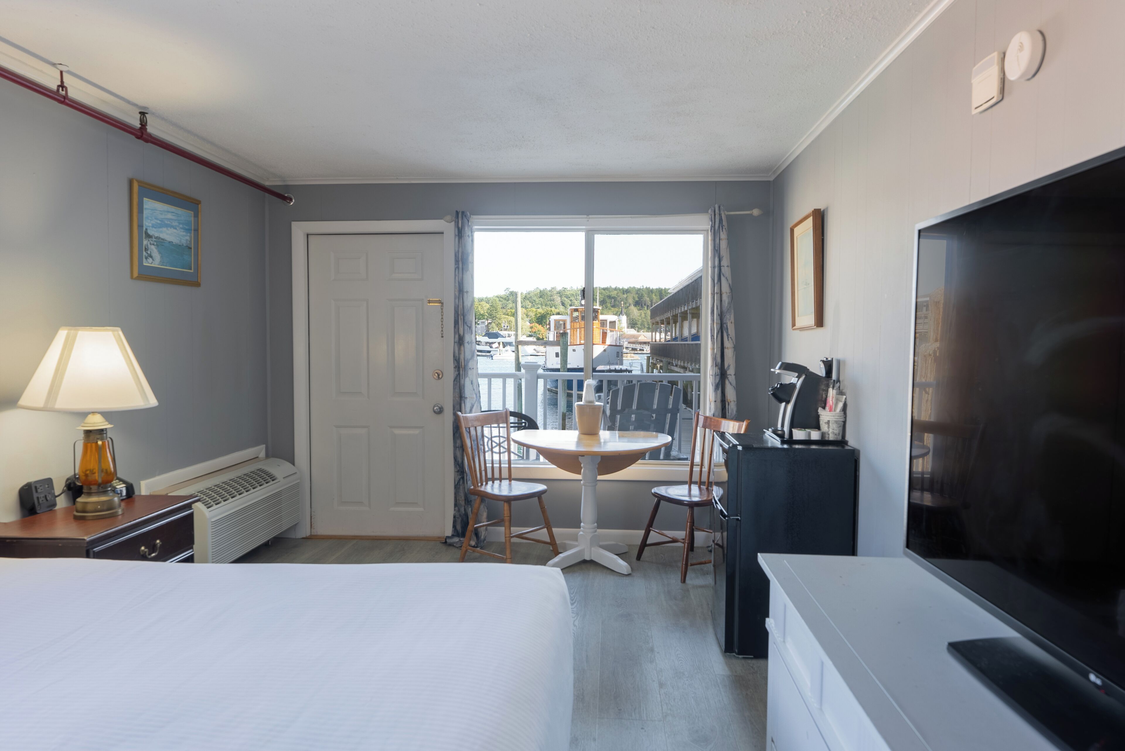 A hotel room with a bed, a table with chairs, a TV, and a window with a view of buildings and trees.