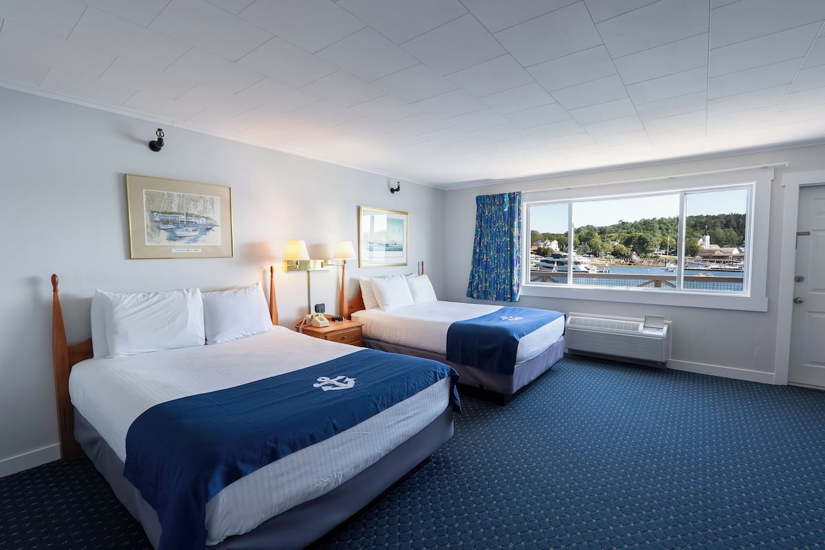 A hotel room with two beds, a large window with a view of a marina, and a framed picture on the wall.