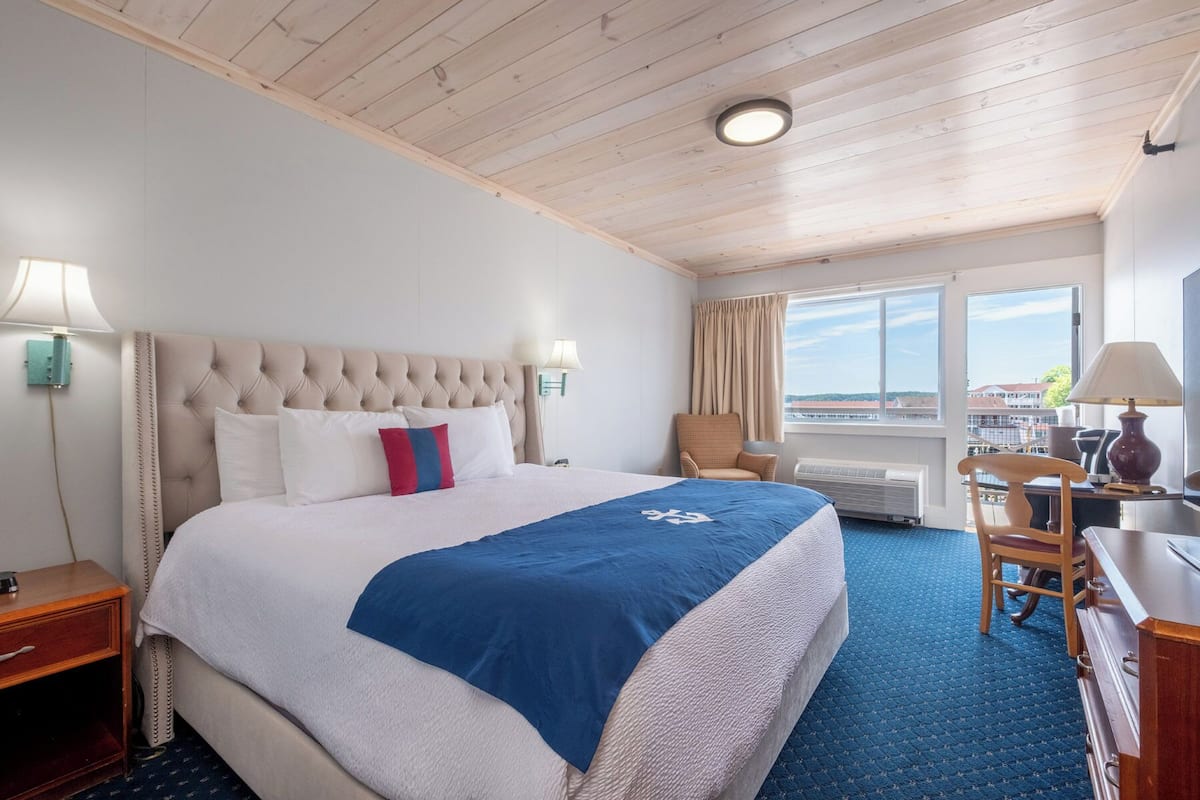A hotel room with a large bed, a desk, a chair, and a view of the outside.