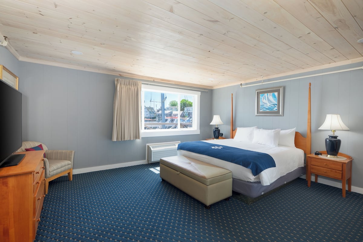 A hotel room with a large bed, a desk, a chair, a window with a view of buildings, and a painting on the wall.