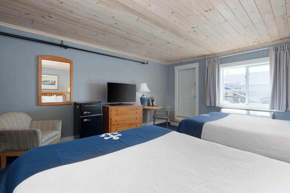 A hotel room with two beds, a TV, a dresser, a chair, and a window with a view.