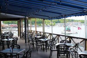 An outdoor dining area with tables and chairs, overlooking a body of water with boats and buildings in the background. - Fishermans Wharf Inn (Boothbay Harbor)
