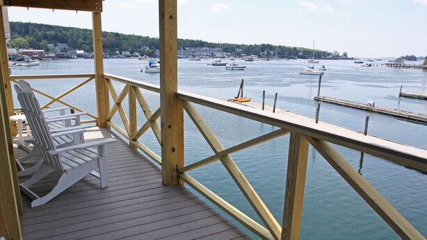 Eine Holzterrasse mit weißen Stühlen mit Blick auf eine Marina und Boote.