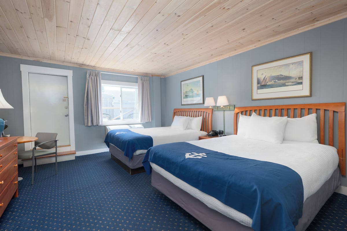 A hotel room with two beds, a desk, a chair, and a window with curtains.