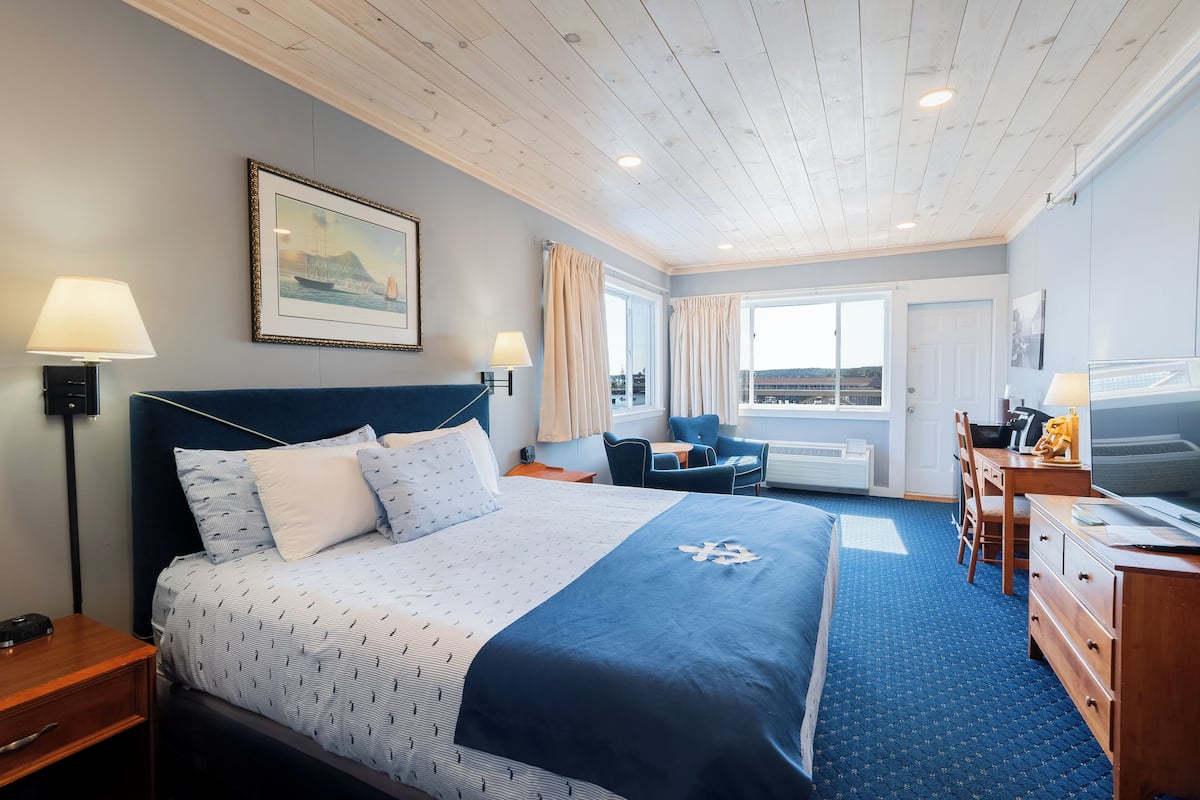 A hotel room with a bed, bedside lamps, a desk with a chair, a TV, and a window with curtains.