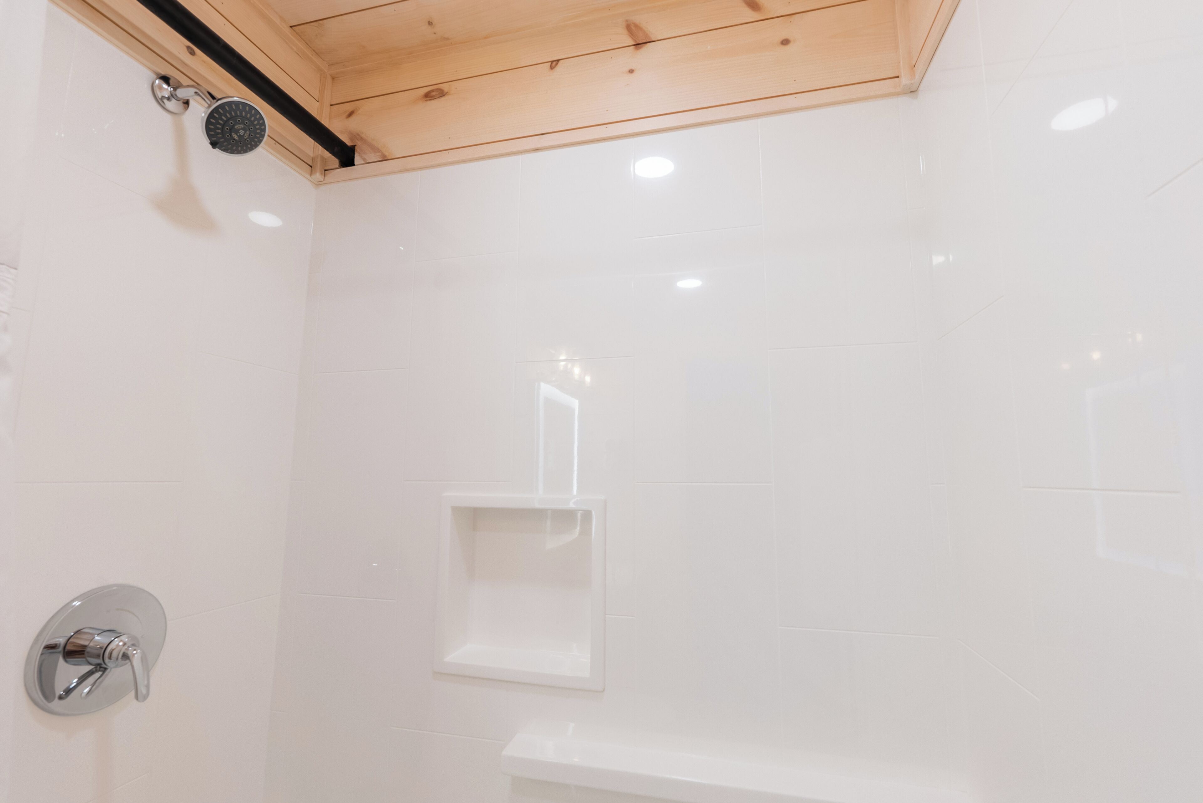 Un espacio de ducha con azulejos blancos, techo de madera y un pequeño estante.