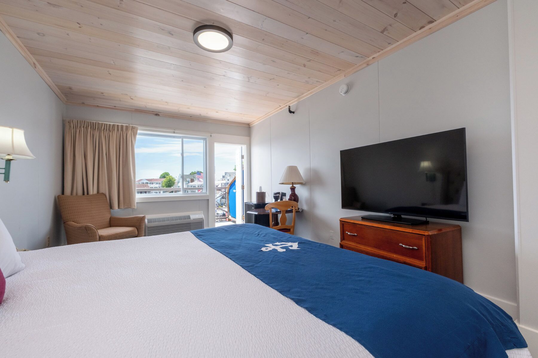 Habitació d'hotel amb llit, televisió, cadira, escriptori i finestra amb vista.