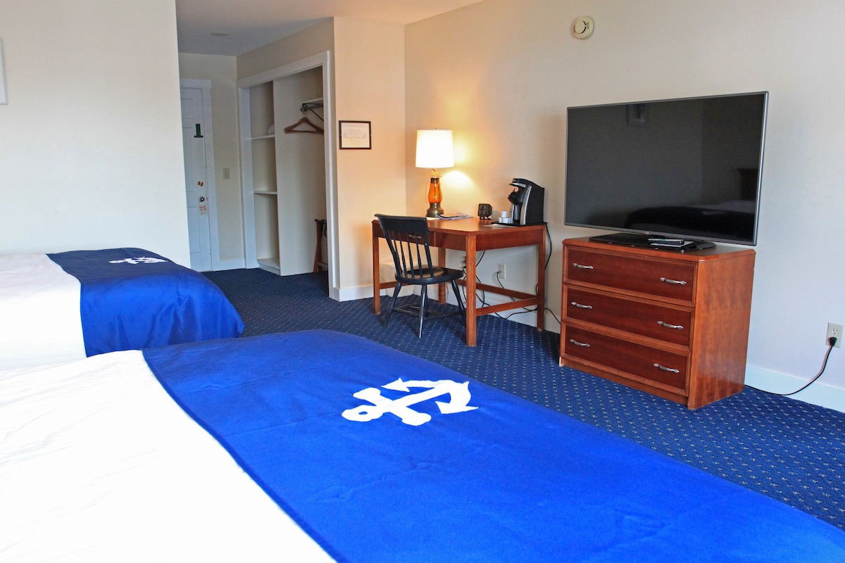 A hotel room with two beds, a desk with a lamp, a TV, and a dresser.
