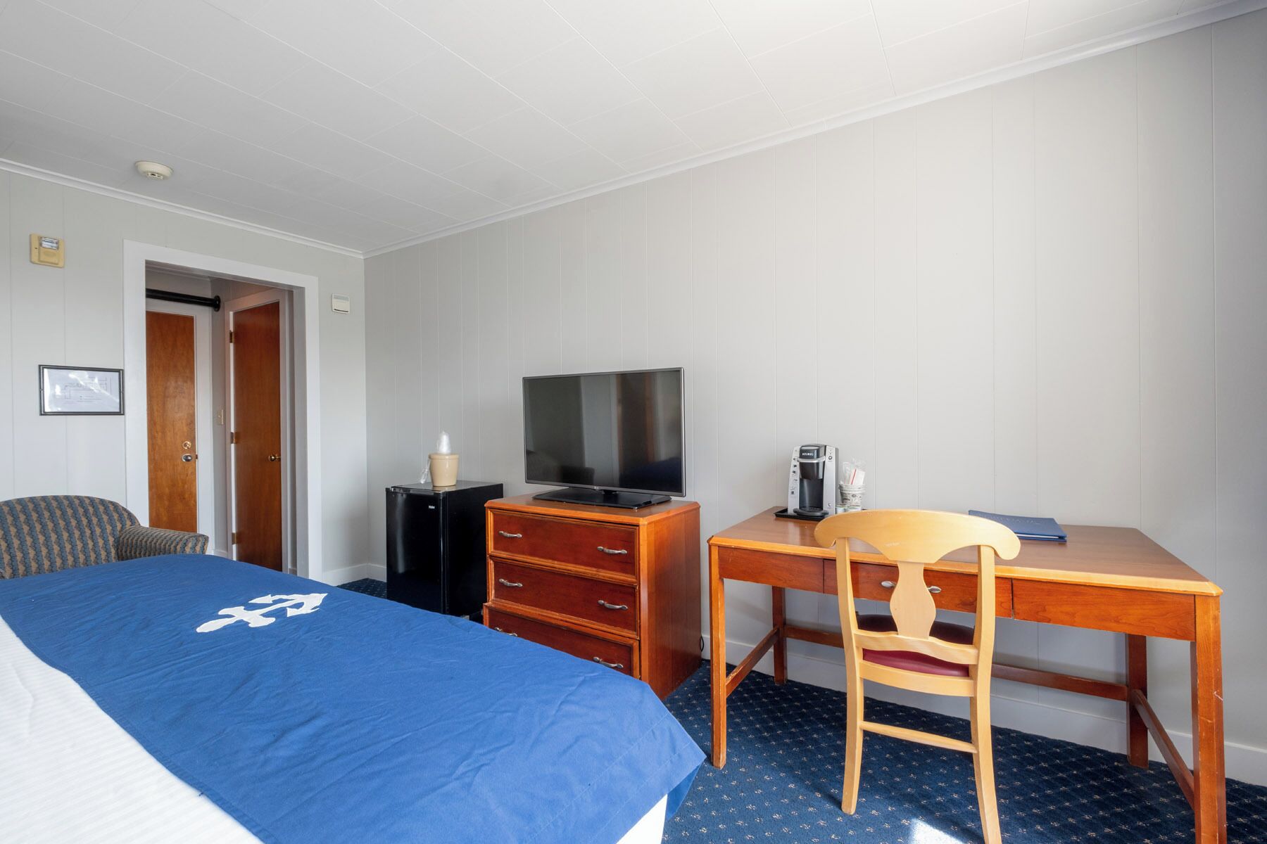 A hotel room with a bed, a desk, a chair, a television, and a coffee maker.