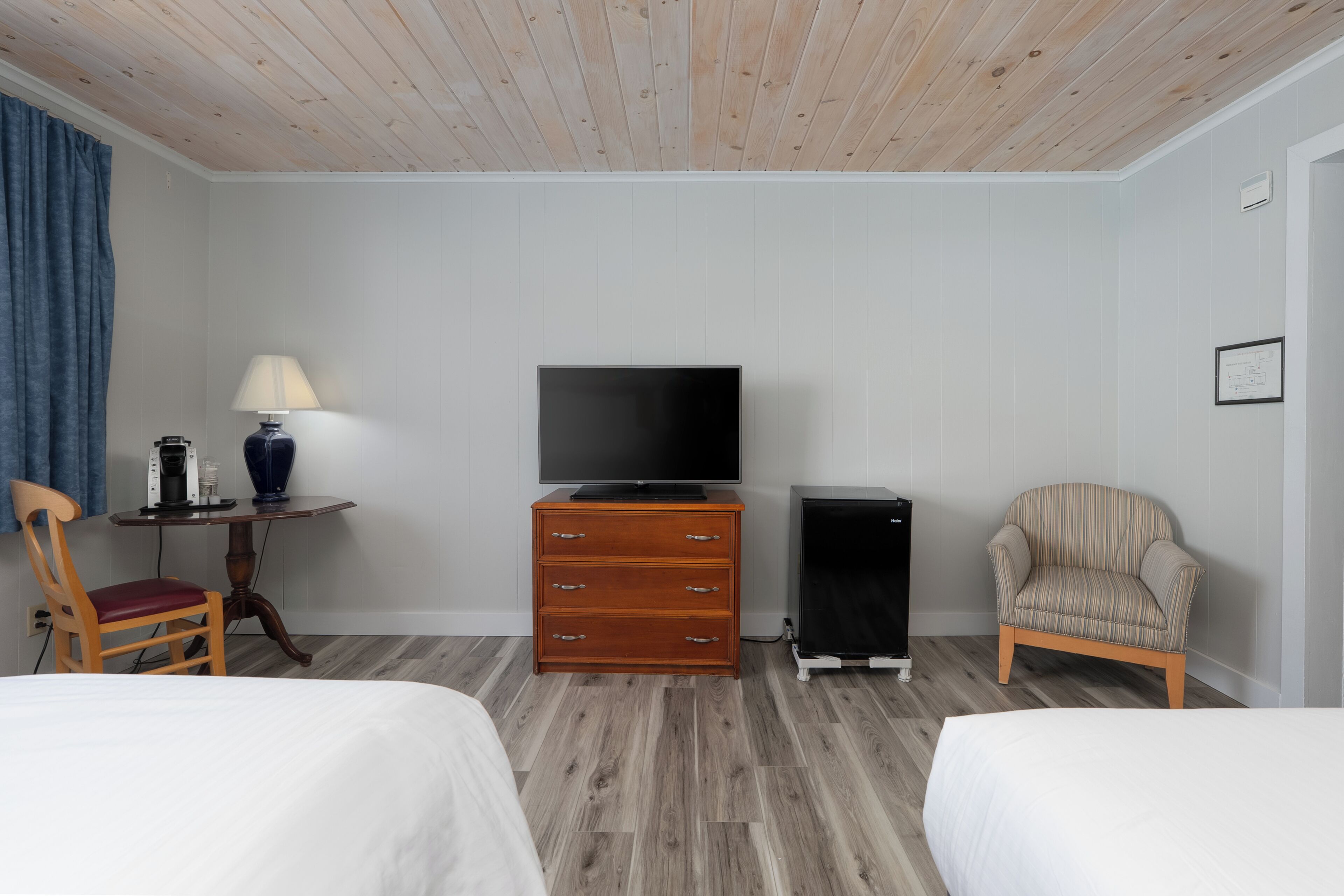 A hotel room with two beds, a TV, a dresser, a chair, and a small table with a lamp.