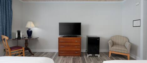 A hotel room with two beds, a TV, a dresser, a chair, and a small table with a lamp.