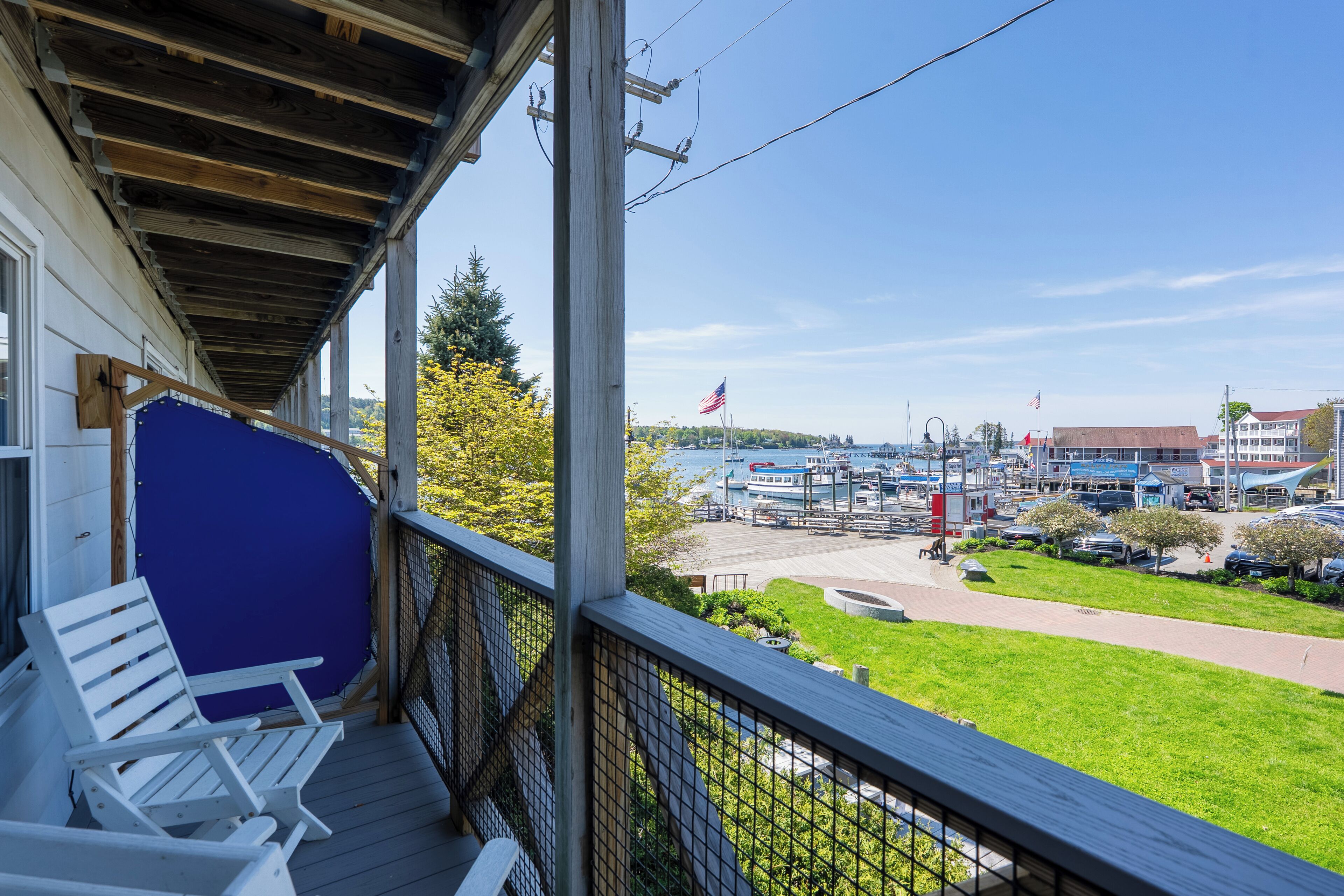 A wooden deck with two white chairs, overlooking a marina with boats and a clear blue sky.