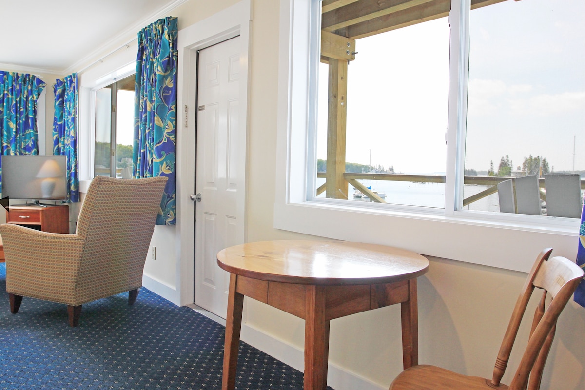A room with a wooden table and a chair, a television, and a window with a view of a dock and water.