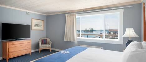 Ein Hotelzimmer mit Bett, Fernseher, Sessel, Fenster mit Blick auf ein Gewässer und einer Lampe.