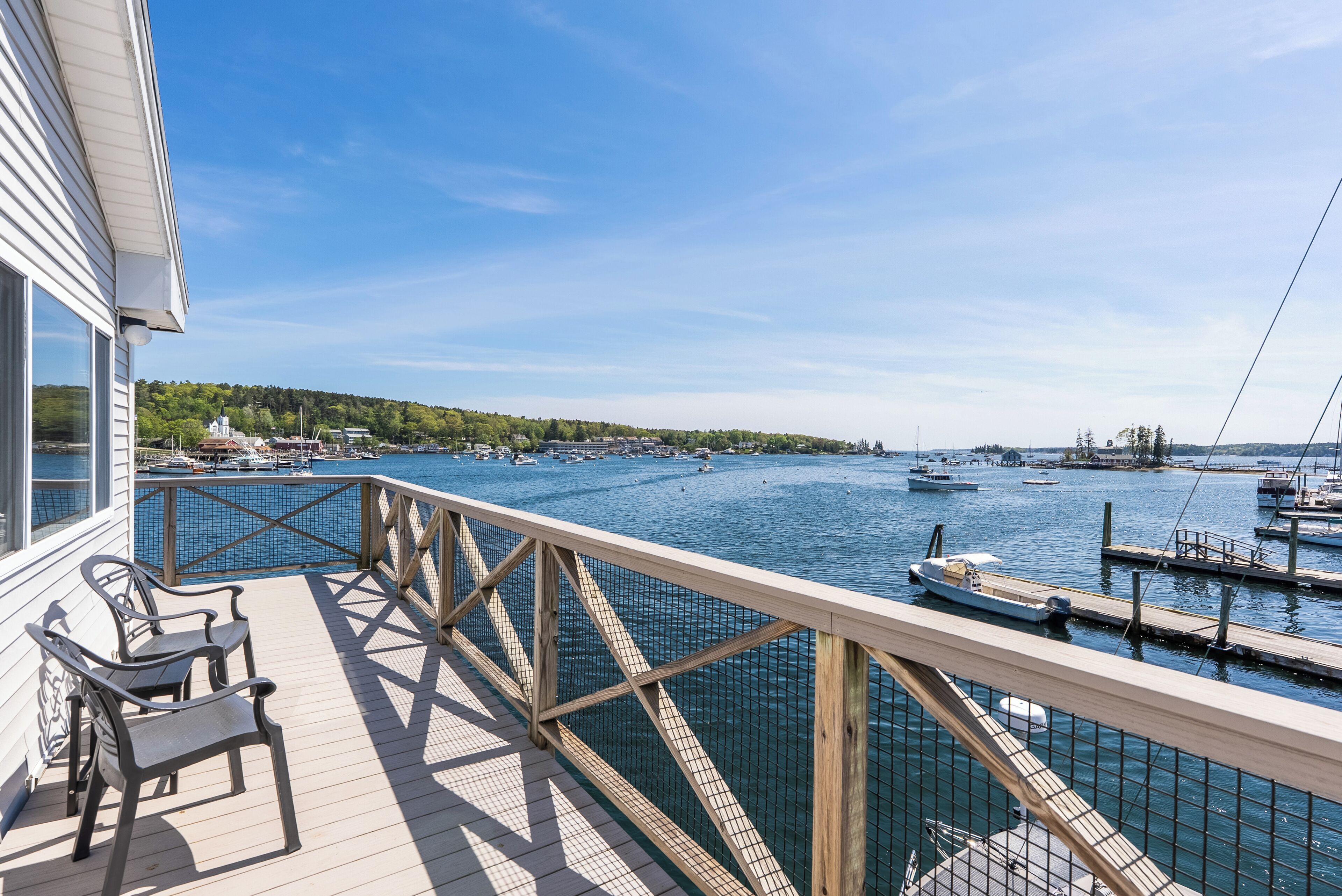 A wooden deck with chairs, overlooking a marina with boats and a clear blue sky.
