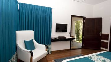 Un dormitorio con una silla blanca, una cama con colcha azul y blanca, un televisor en la pared y una puerta de madera.