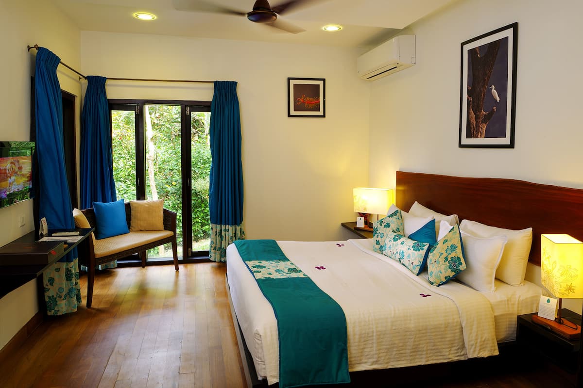 A hotel room with a bed, bedside tables, a desk, a chair, a ceiling fan, and a window with curtains.