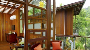 Une terrasse en bois avec deux chaises et une table, un mur en bois avec une fenêtre, et une vue sur la verdure.