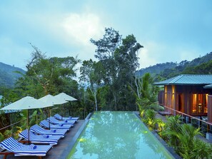 A pool with lounge chairs and umbrellas, surrounded by lush greenery and a mountain backdrop. - Niraamaya Cardamom Club (Peermade)