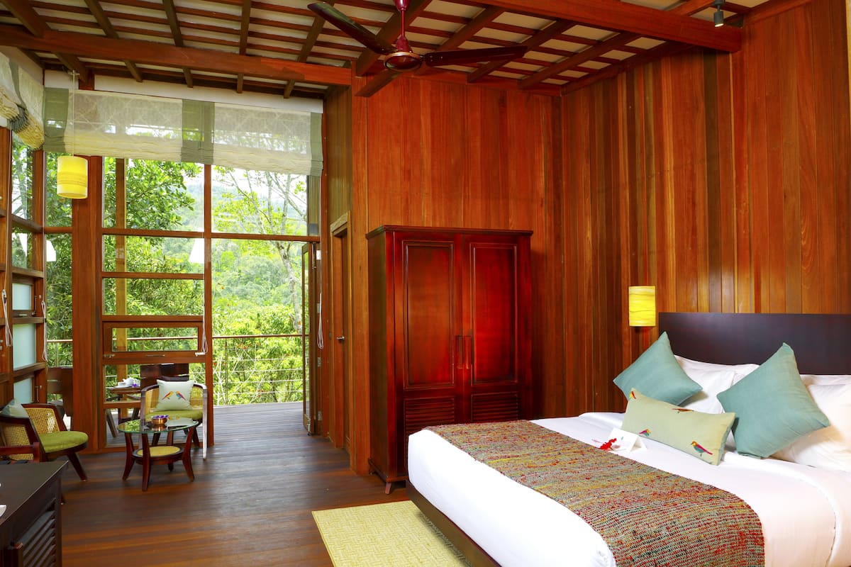 A spacious bedroom with a large bed, a wooden wardrobe, and a balcony with a view of greenery.